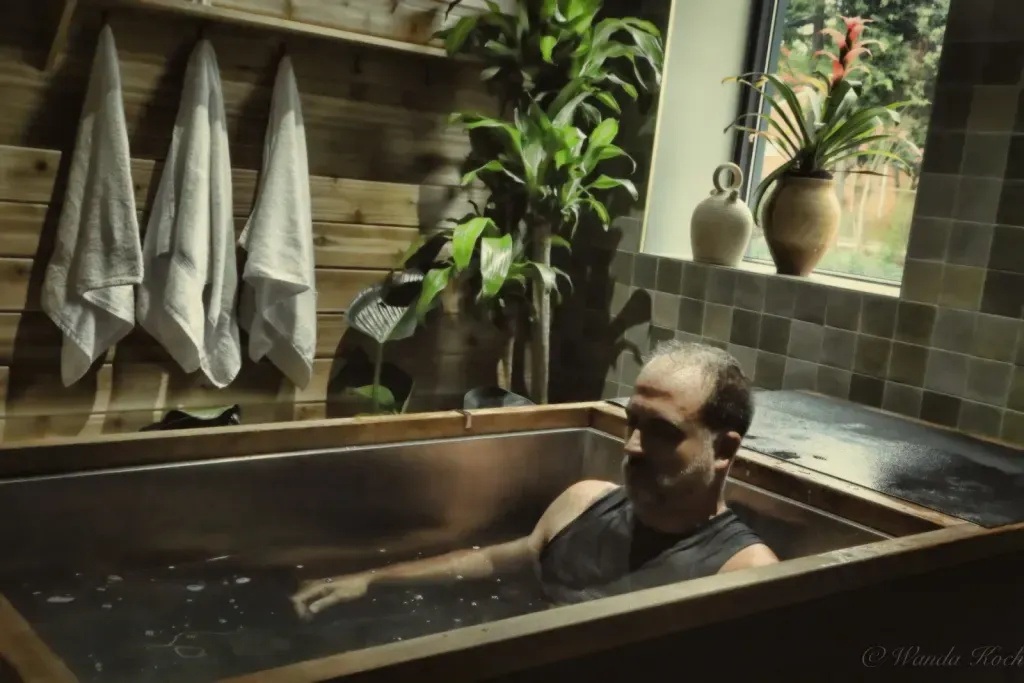 Bearded man relaxing in an individual wood-framed cold plunge with towels and plants at Sauna Culture Charlotte