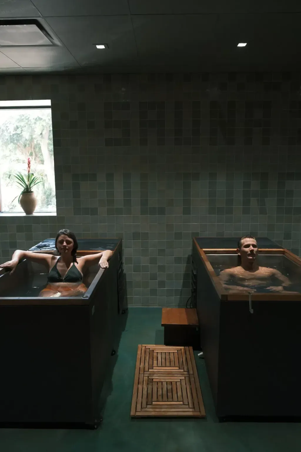Two guests in individual cold plunges with the Sauna Culture tile mural in Charlotte