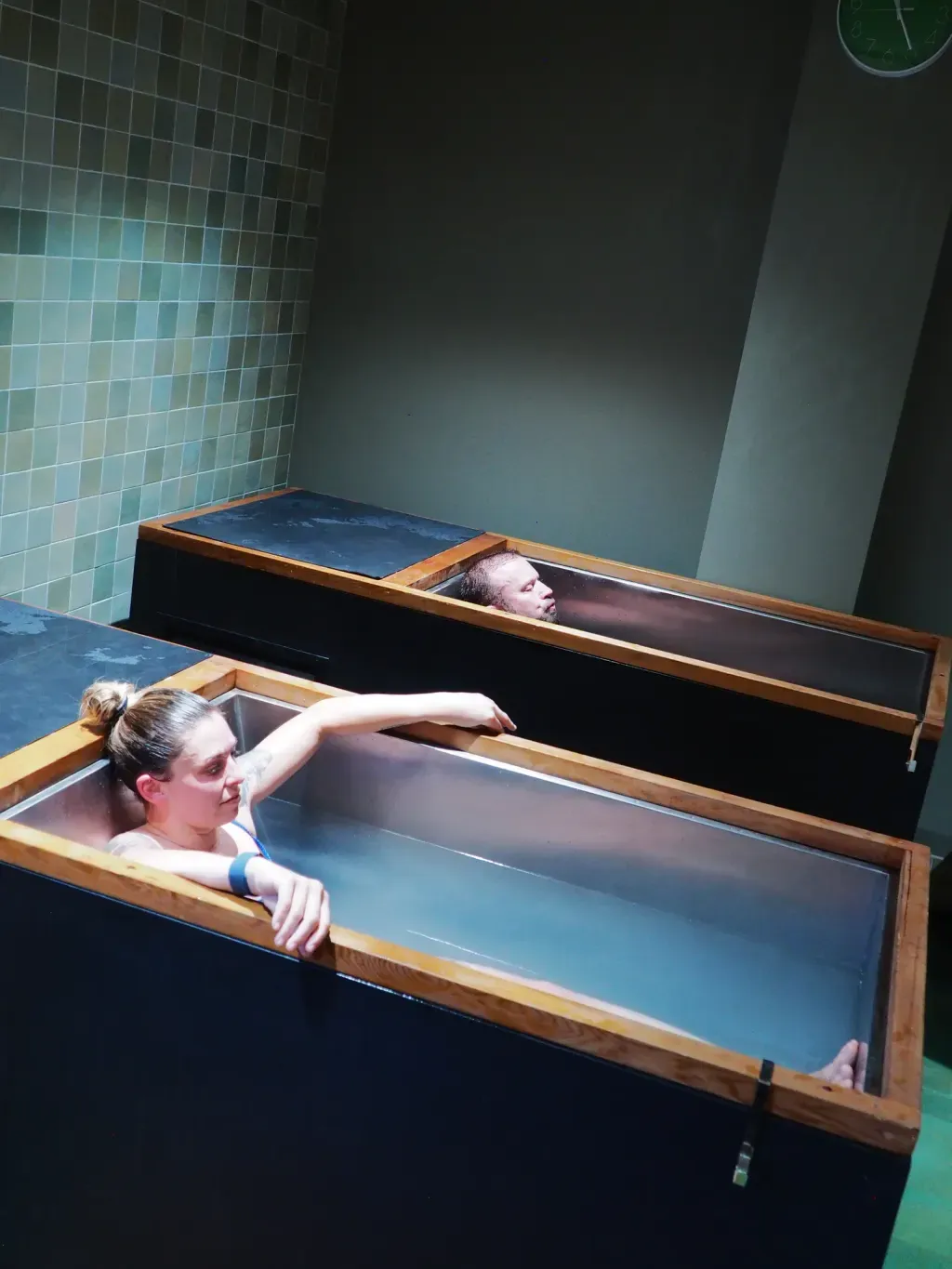 Husband and wife in side-by-side individual cold plunges at Sauna Culture in Cotswold, Charlotte