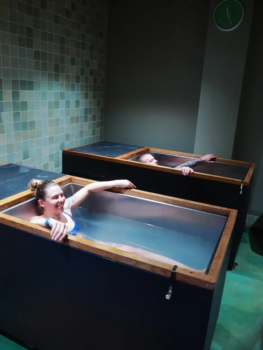 Couple laughing in neighboring individual cold plunges at Sauna Culture Charlotte
