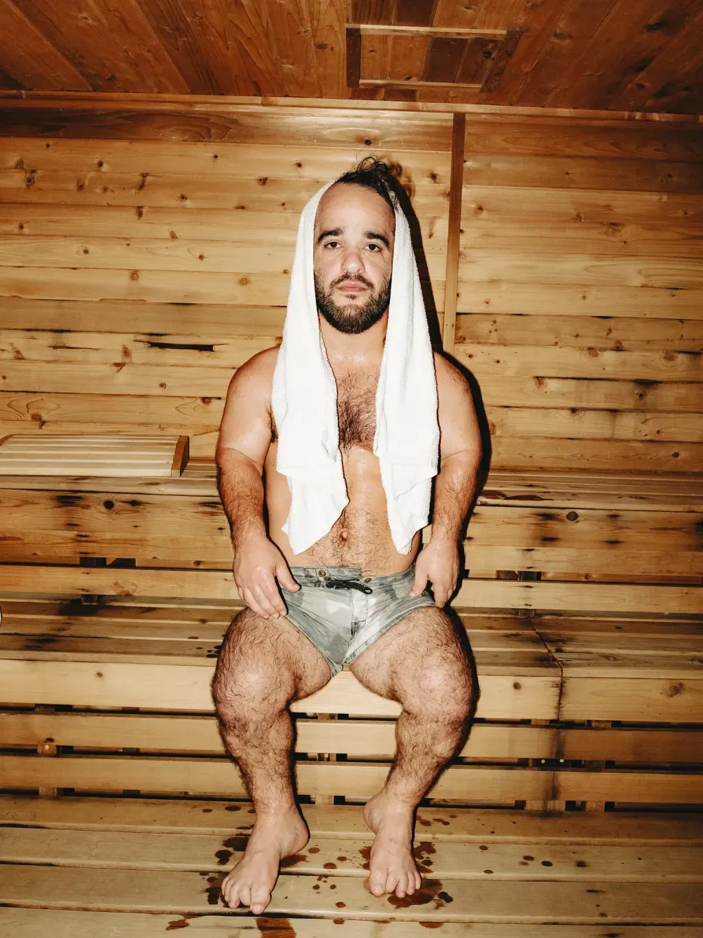 Guest with a towel over his head sitting on a cedar bench in the Finnish sauna at Sauna Culture Charlotte