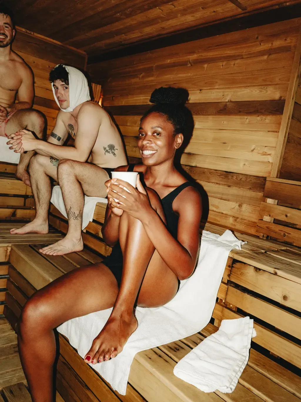 Guest smiling with a cup on the cedar bench of the Finnish sauna at Sauna Culture Charlotte, friends behind her