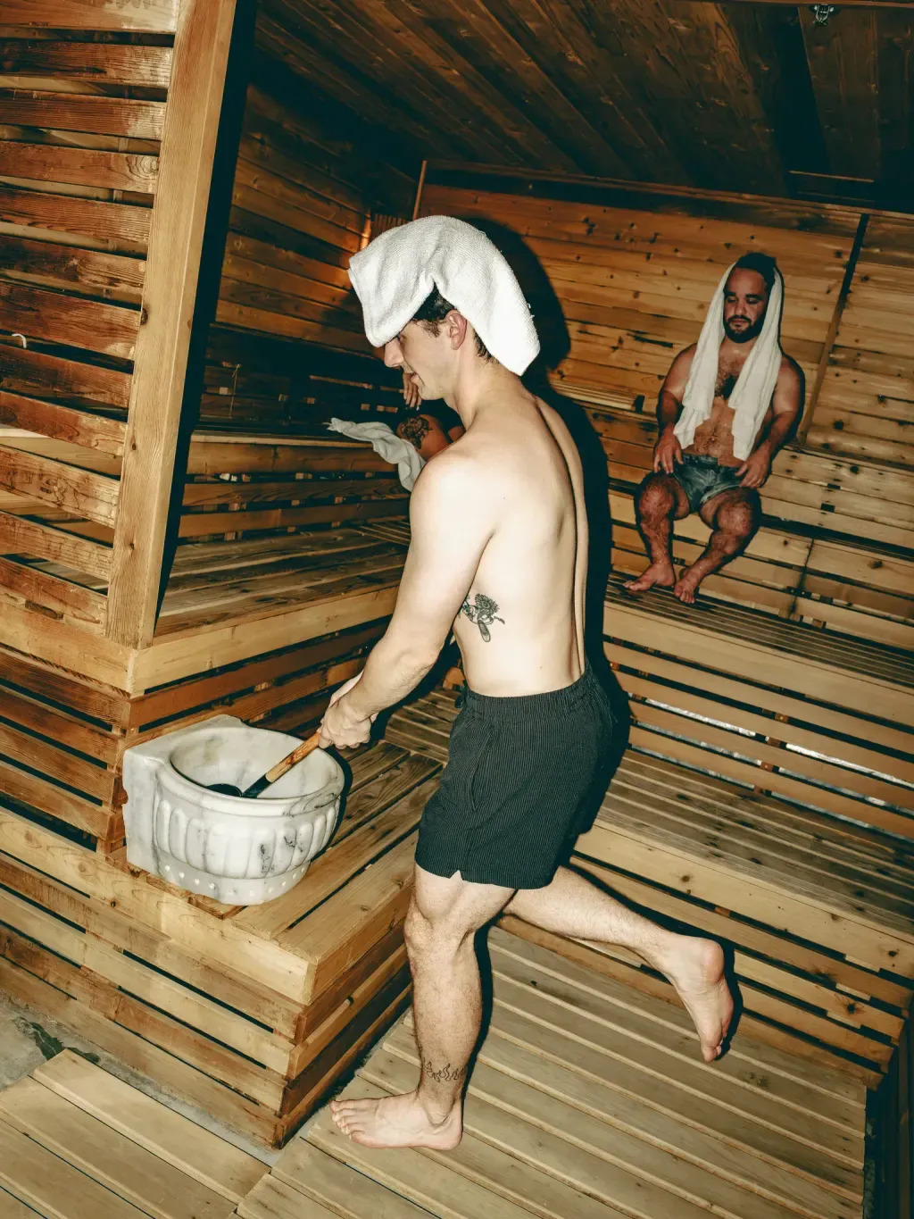 Guest scooping water with a wooden ladle for löyly in the Finnish sauna at Sauna Culture Charlotte