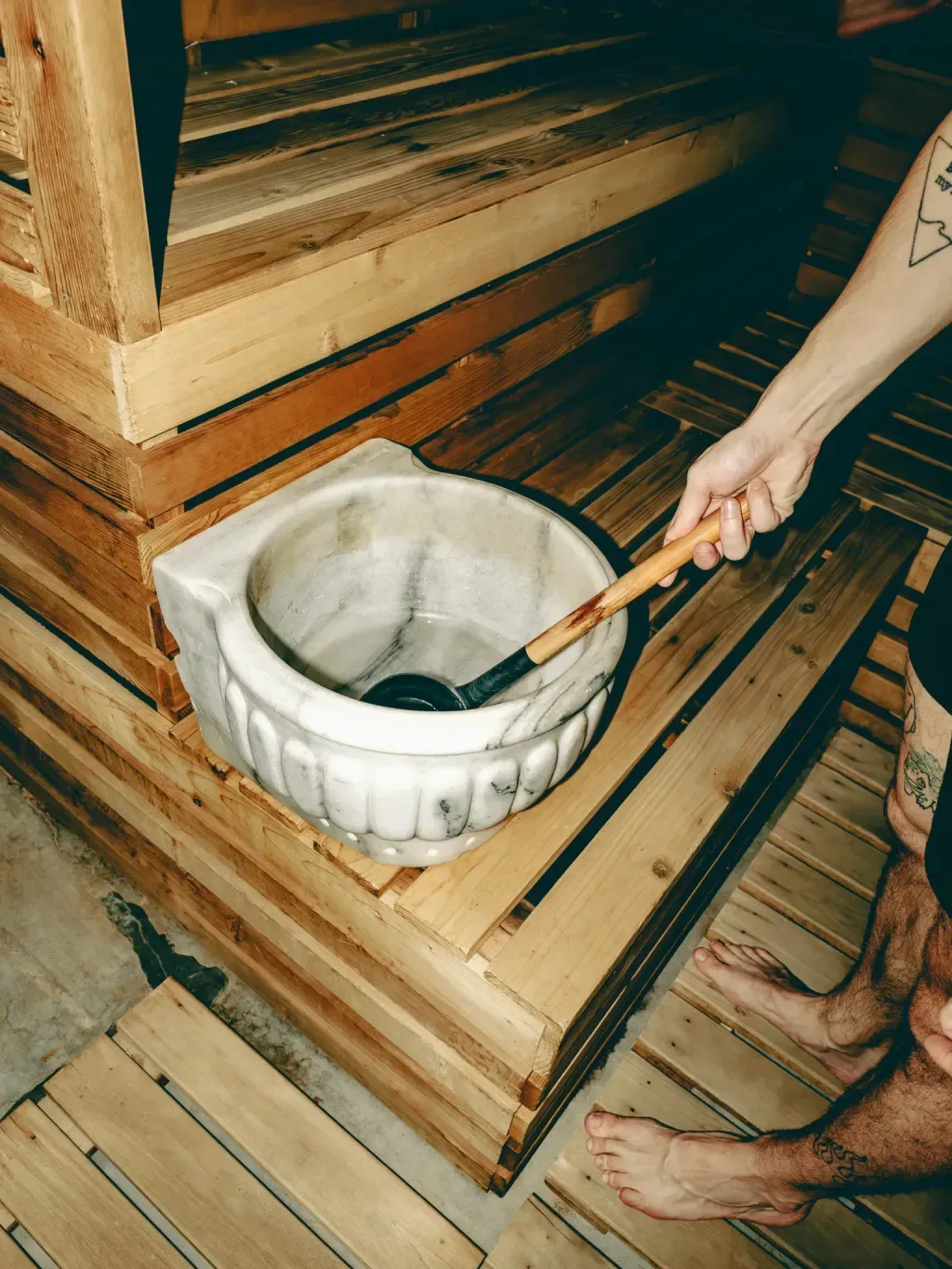 White marble basin and wooden ladle on the cedar bench of the Finnish sauna at Sauna Culture Charlotte