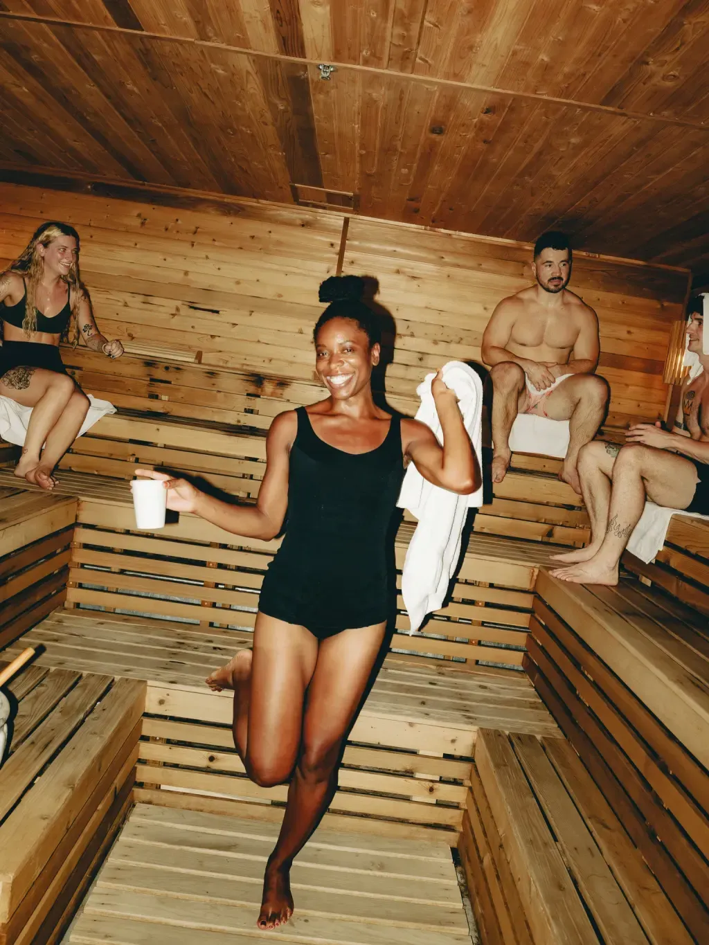 Guest standing and smiling in the communal Finnish sauna at Sauna Culture Charlotte, friends on the benches