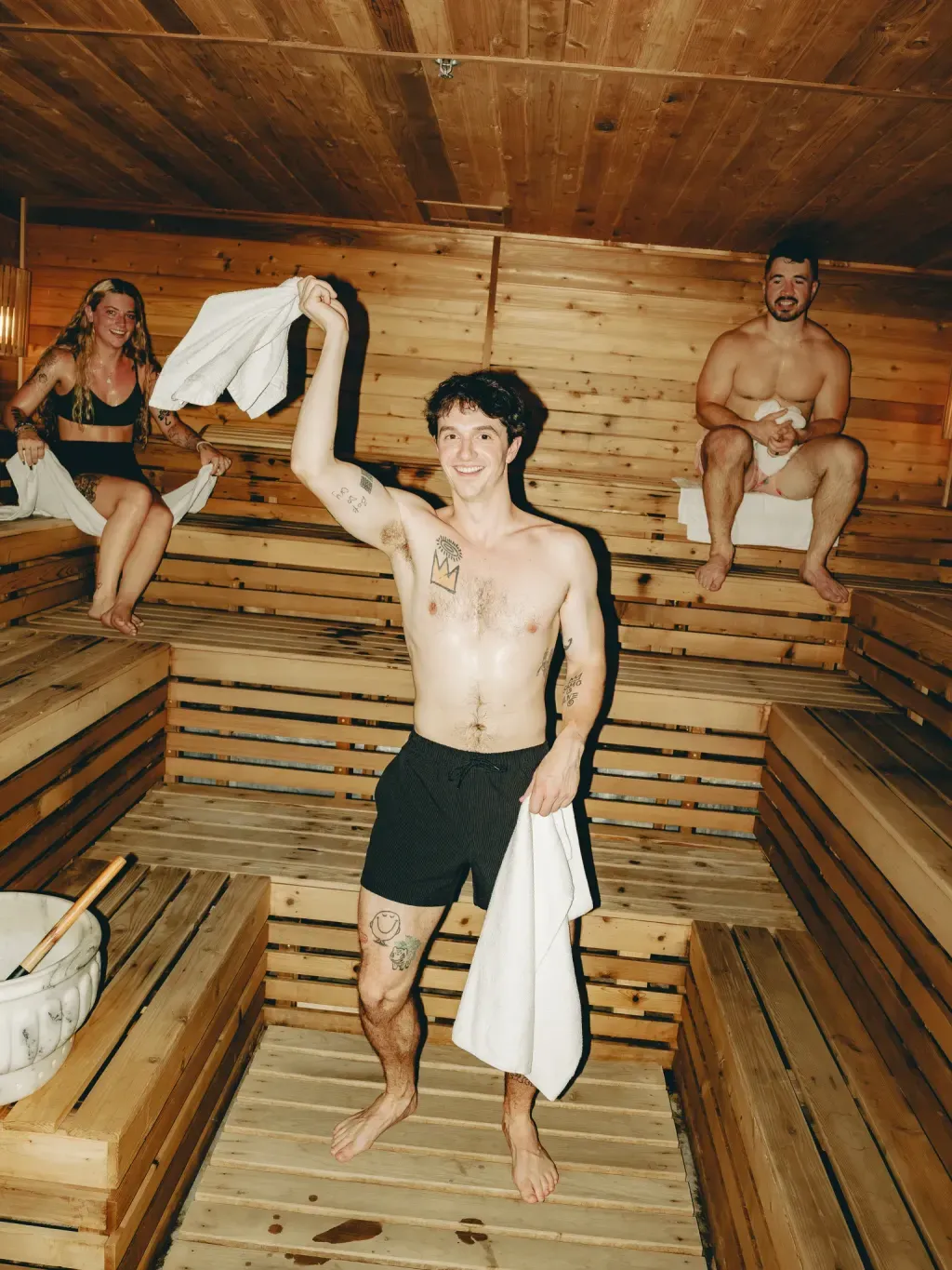 Three guests in the cedar Finnish sauna at Sauna Culture Charlotte, one holding a towel overhead