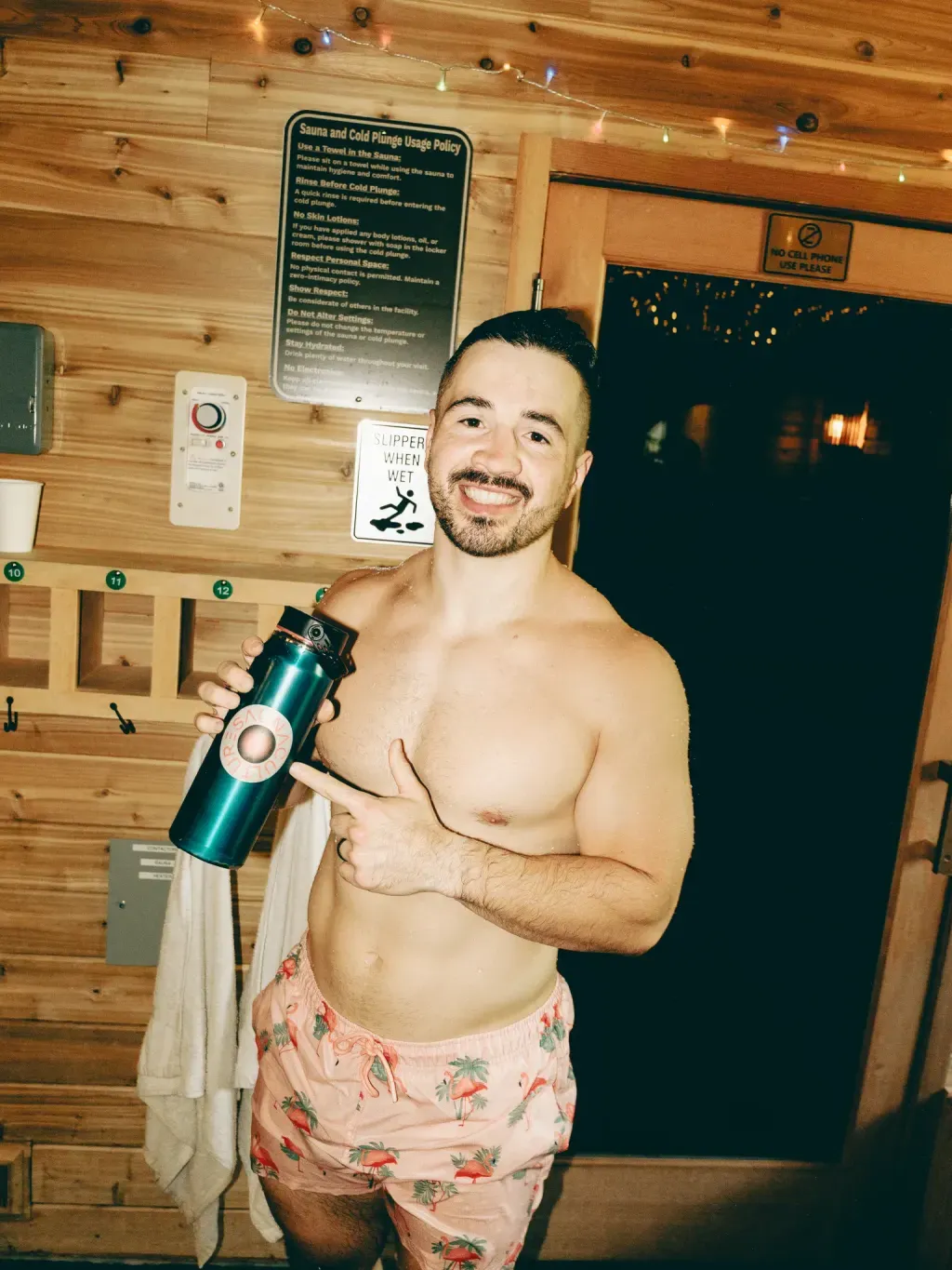 Guest in the studio lobby with a water bottle beside the sauna and cold plunge usage policy at Sauna Culture Charlotte