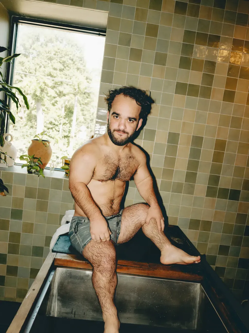 Guest sitting on the wood rim of an individual cold plunge by the window at Sauna Culture Charlotte