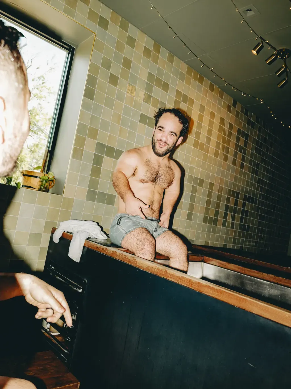 Guest smiling on the edge of an individual cold plunge while talking with a friend at Sauna Culture Charlotte