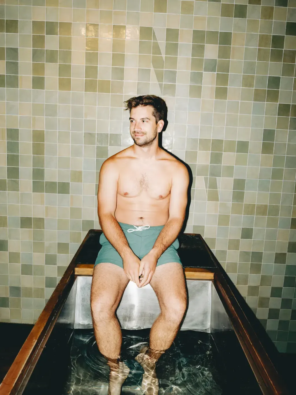 Guest with feet in an individual cold plunge in front of the tiled SAUNA lettering at Sauna Culture Charlotte