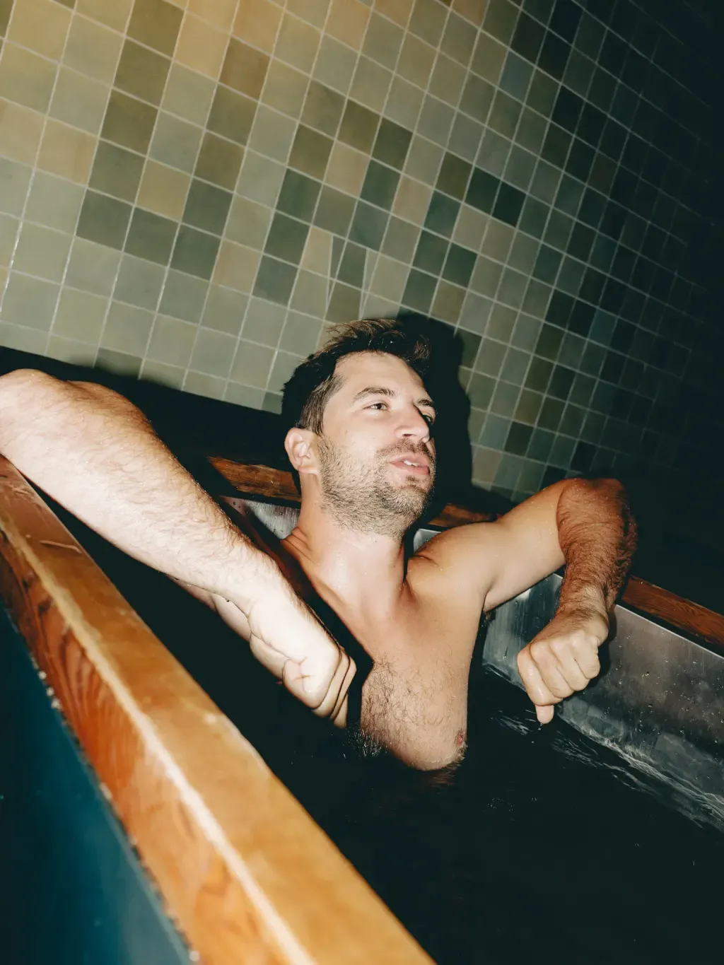 Guest focusing through an individual cold plunge with arms along the cedar rim at Sauna Culture Charlotte