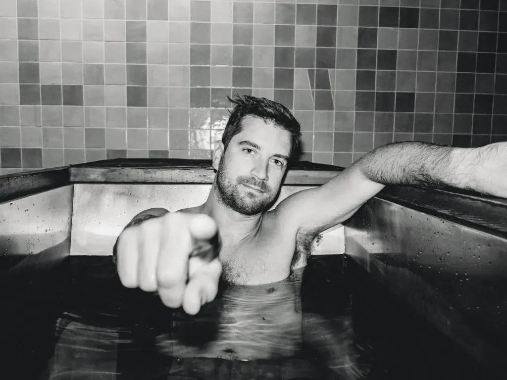 Black-and-white landscape of a guest pointing from an individual cold plunge at Sauna Culture Charlotte