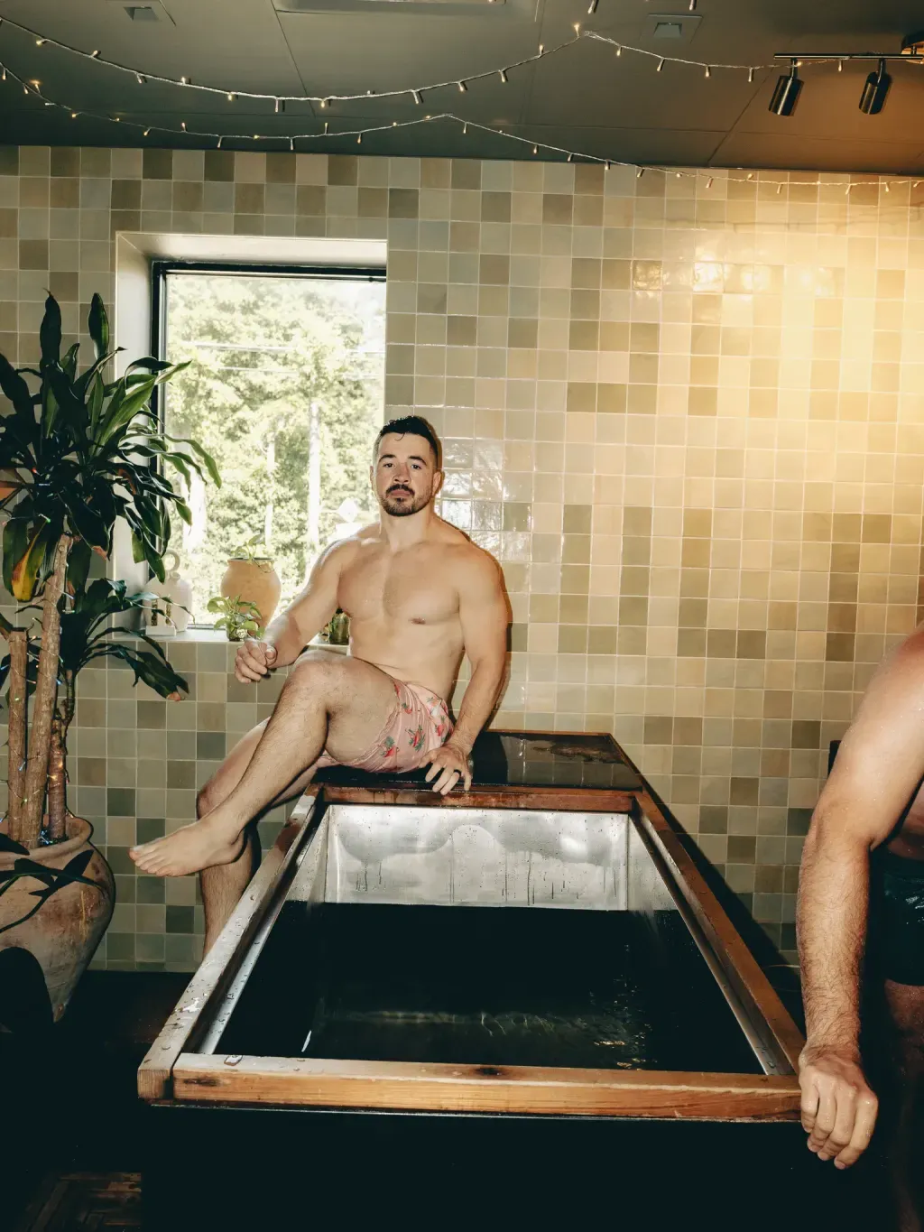 Guest sitting on the corner of an individual cold plunge beside a studio plant at Sauna Culture Charlotte