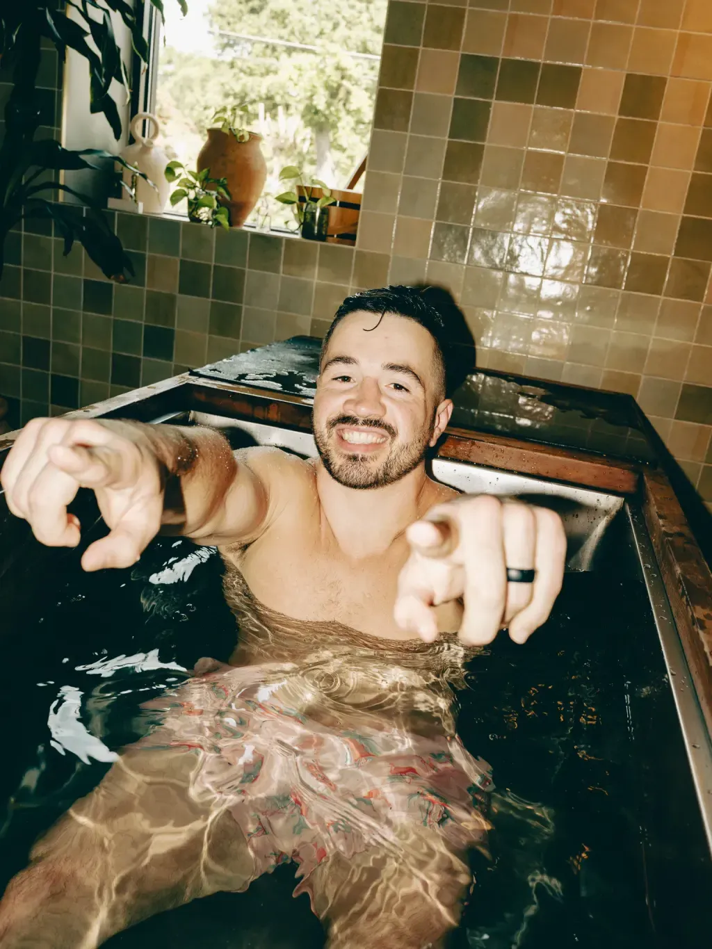 Guest smiling and pointing from an individual wood-rimmed cold plunge at Sauna Culture Charlotte