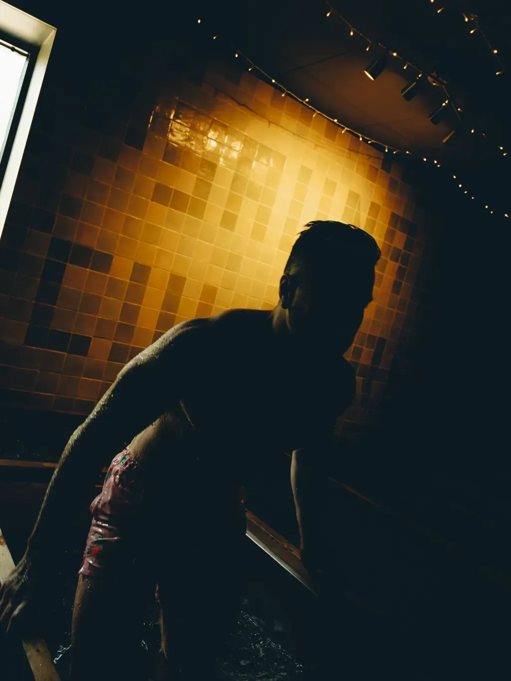 Guest silhouetted at an individual cold plunge under the studio string lights at Sauna Culture Charlotte