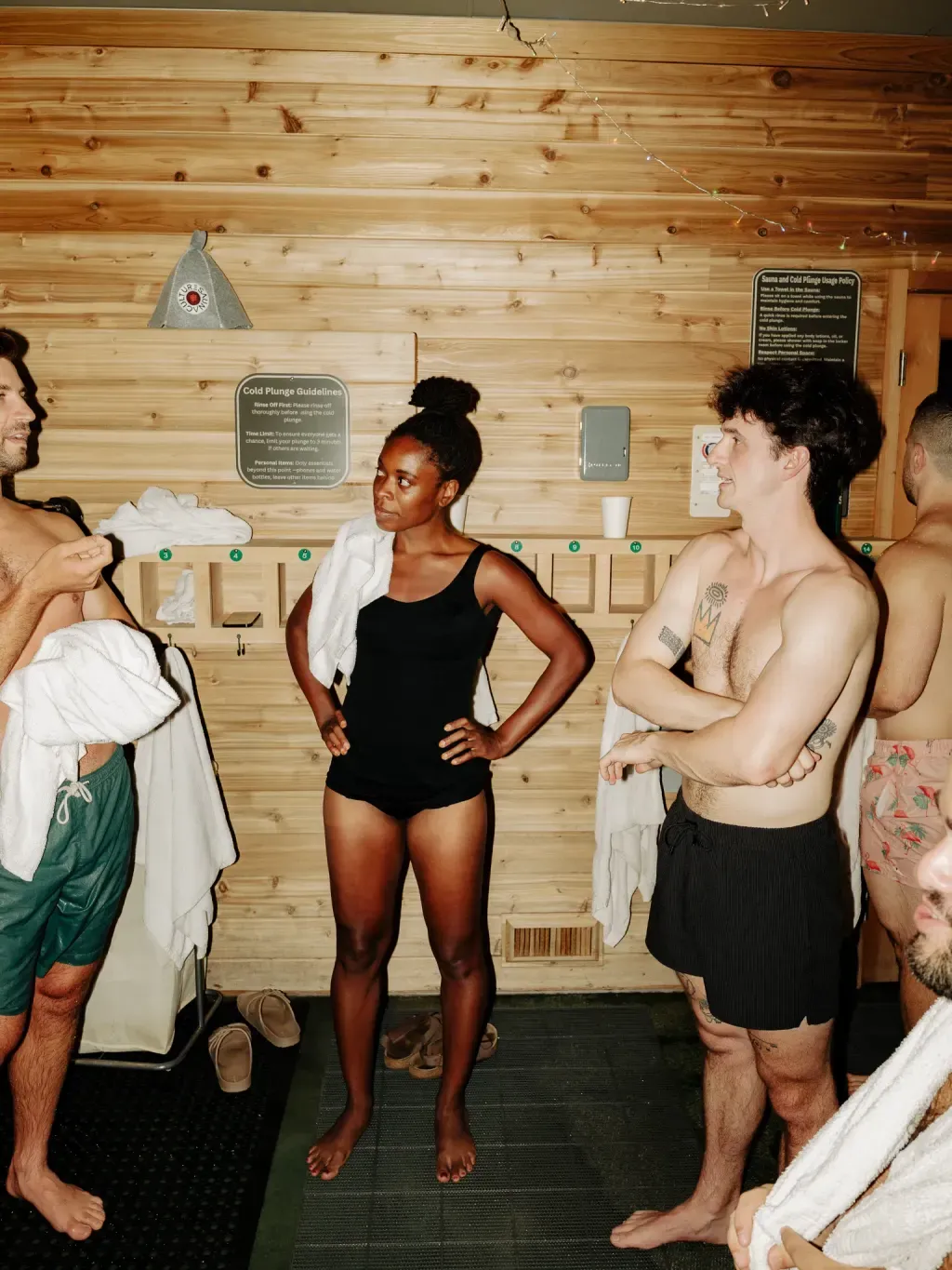 Guests talking by the Cold Plunge Guidelines and towel cubbies at Sauna Culture Charlotte