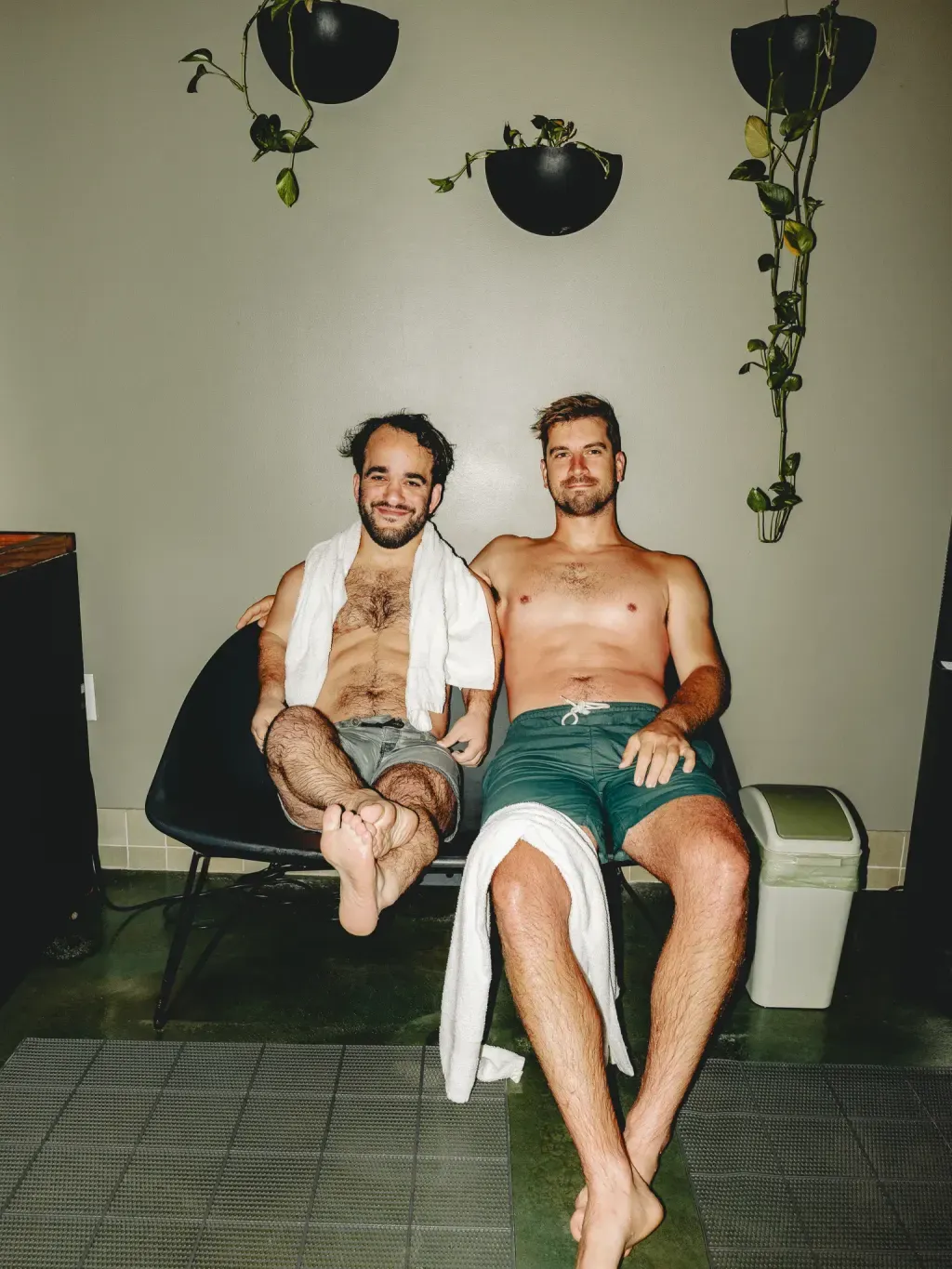 Two guests resting on a lounge chair with hanging plants between rounds at Sauna Culture Charlotte