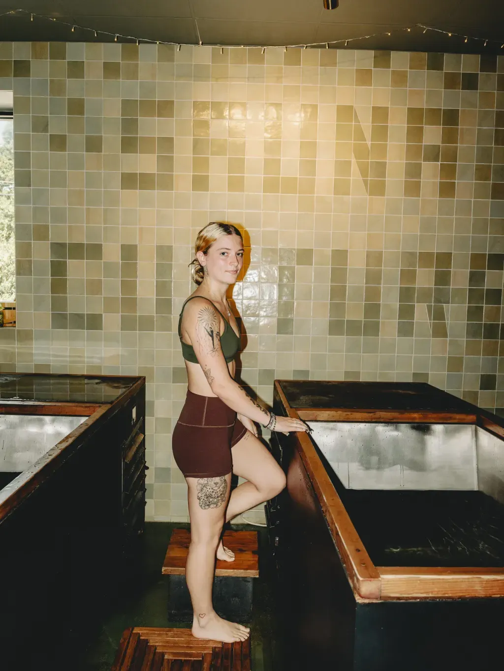 Guest standing between two individual cold plunges in front of the Sauna Culture tile mural in Charlotte