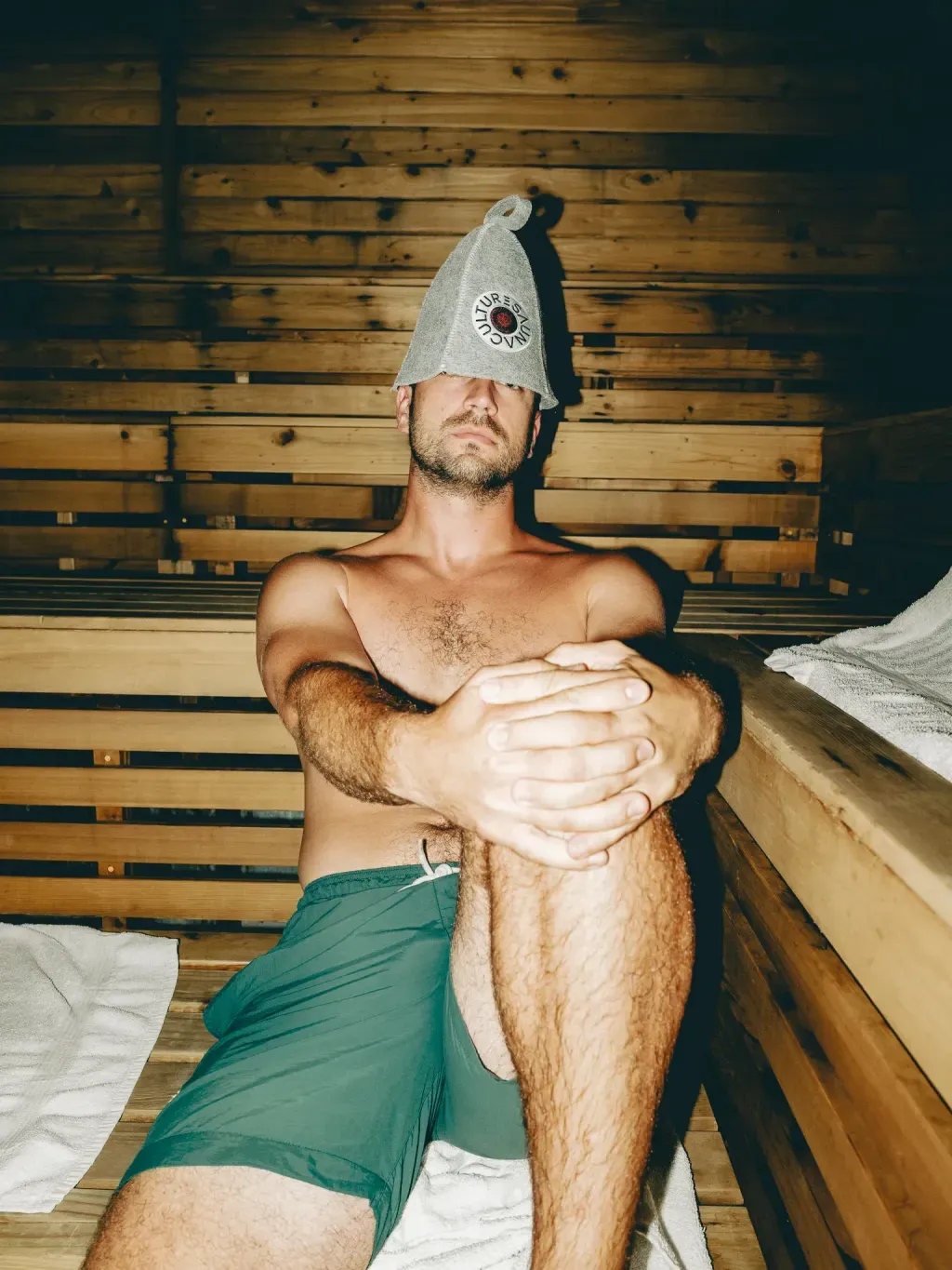 Guest wearing a Sauna Culture felt hat on a cedar bench in the Finnish sauna in Charlotte