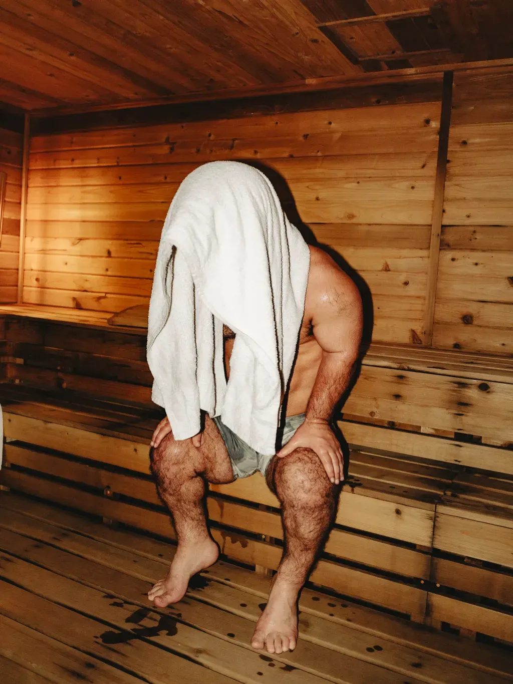 Guest with a towel over his head leaning into the heat of the Finnish sauna at Sauna Culture Charlotte
