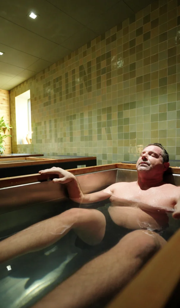 Guest resting chest-deep in an individual cold plunge with the Sauna Culture tile mural at Charlotte's Cotswold studio