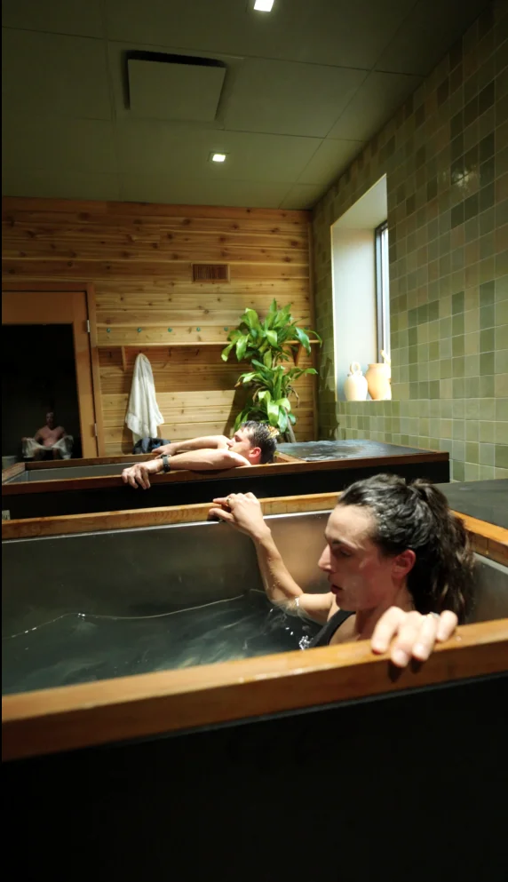 Two guests in individual cold plunges in the cold-plunge room at Sauna Culture, Charlotte